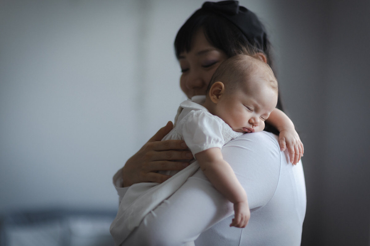 Portrait of a happy family, with parents dressed in white and holding their newborn baby during a photo session at home.