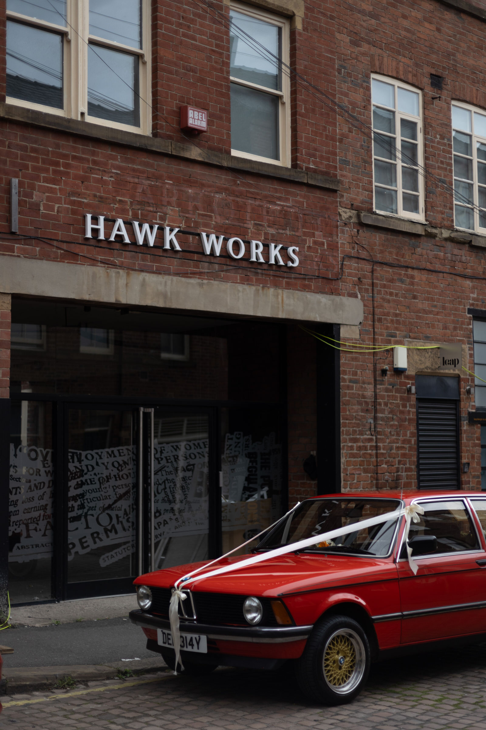 Retro red BMW outside a red brick building with wedding ribbons