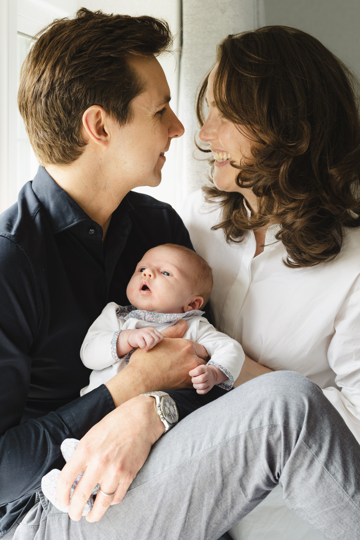 Young dark haired couple looking at each other holding newborn baby