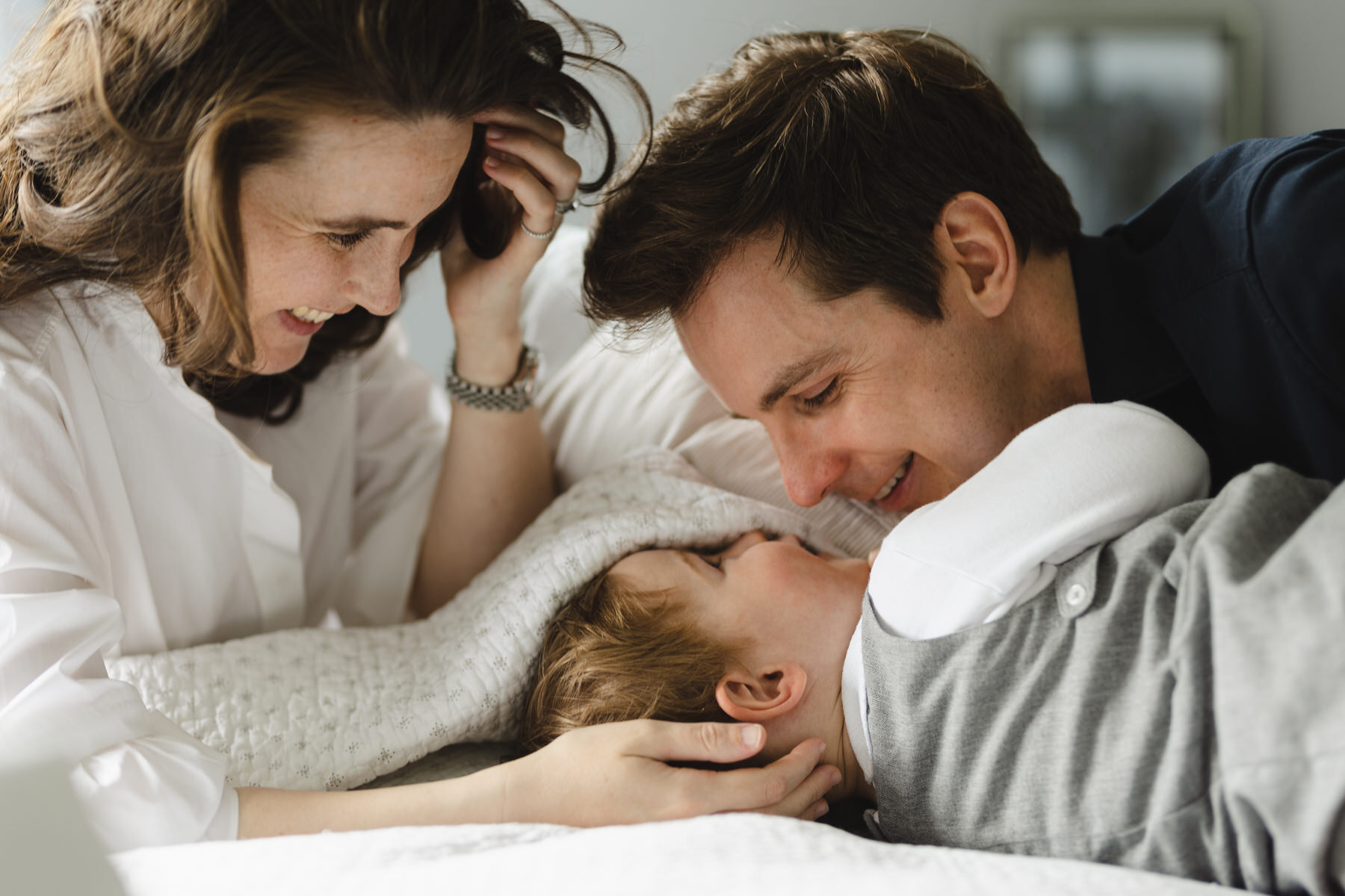 Young Dark haired family wearing white - tickling young son looking happy