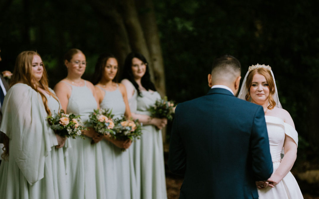 Bride in a white dress smiling and groom in woodland setting with bridesmaids in the background smiling