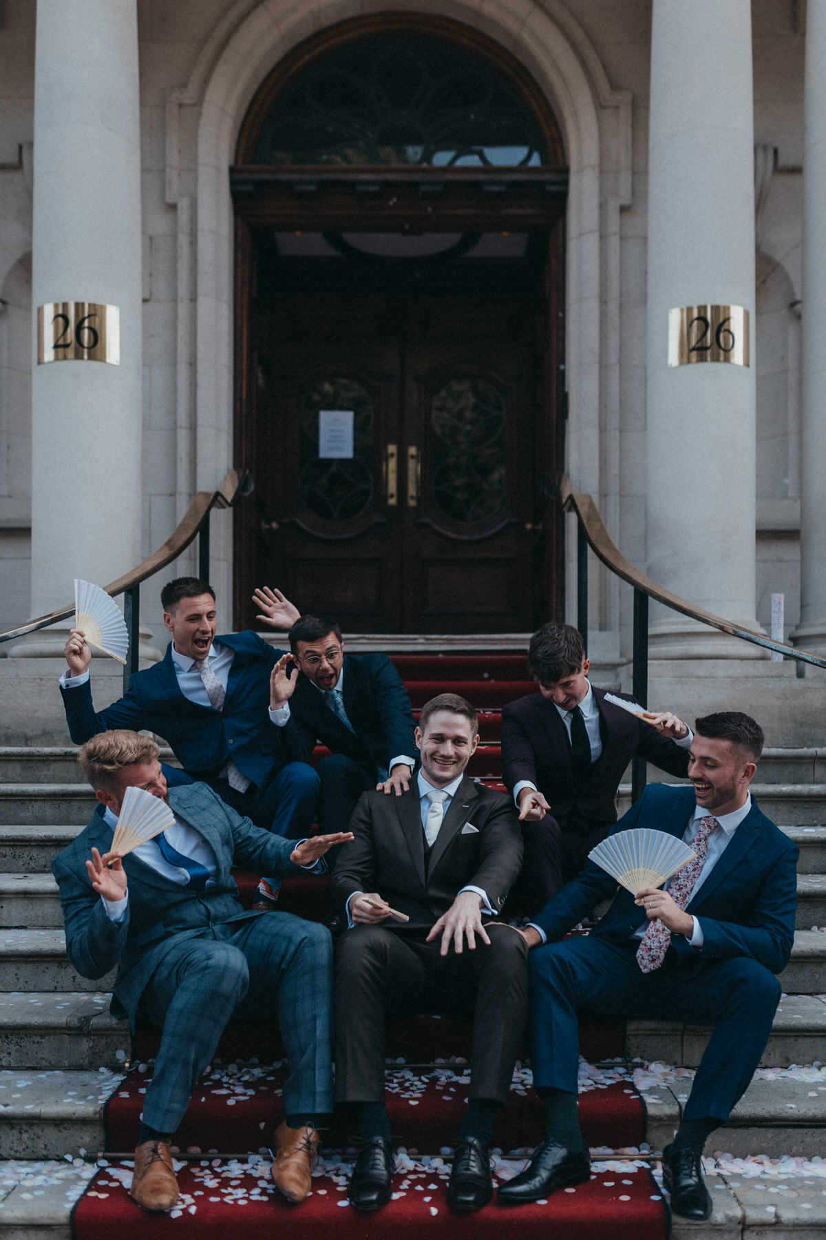 Groomsmen and Groom sitting on red carpet admiring grooms ring