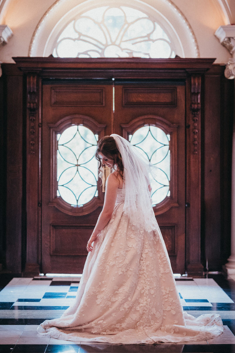 Bride in white gown looking sideways, in front of two large wooden doors in the Roseate Hotel